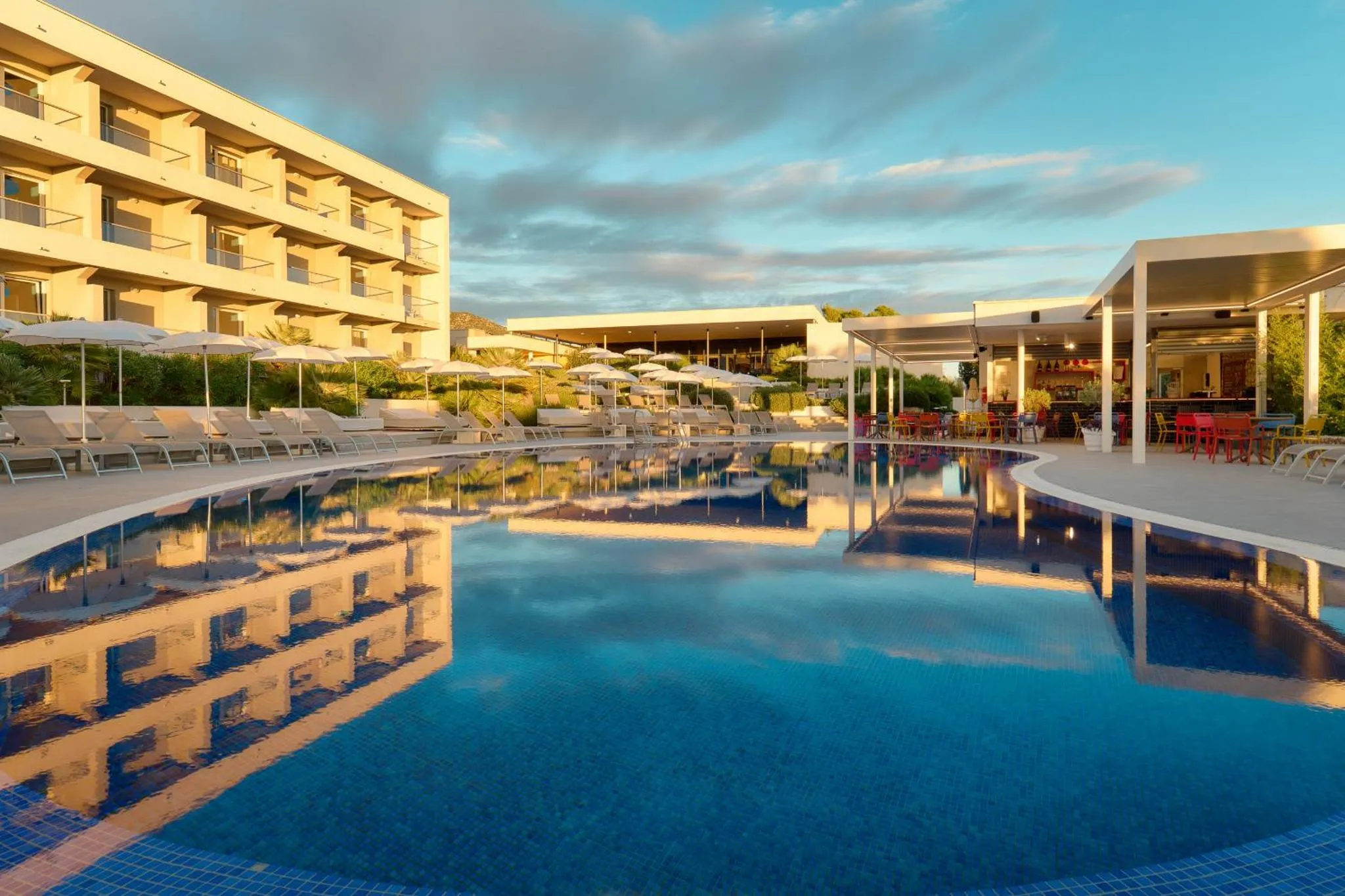 Vue d'une piscine avec des transats et un bar en terrasse devant un bâtiment.