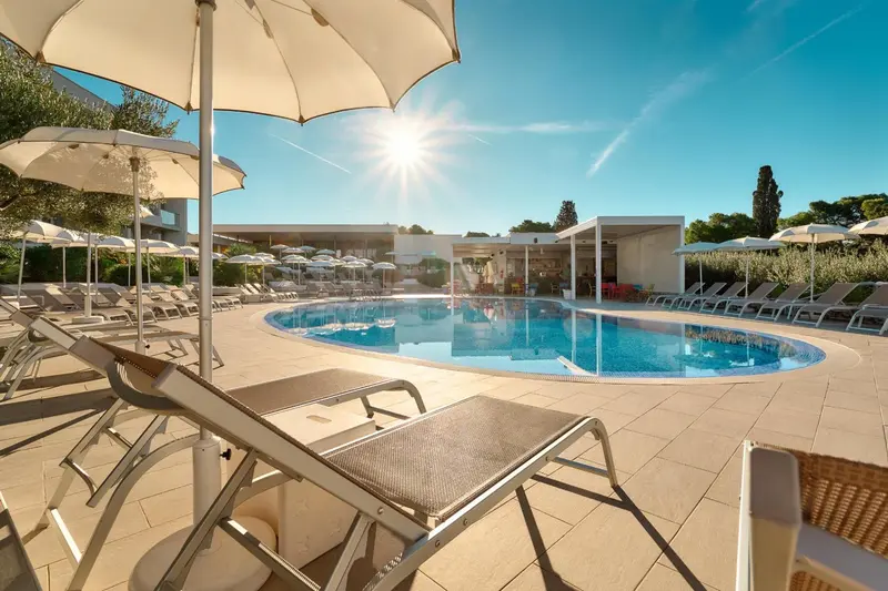 Transats blancs disposés autour d'une piscine ensoleillée.
