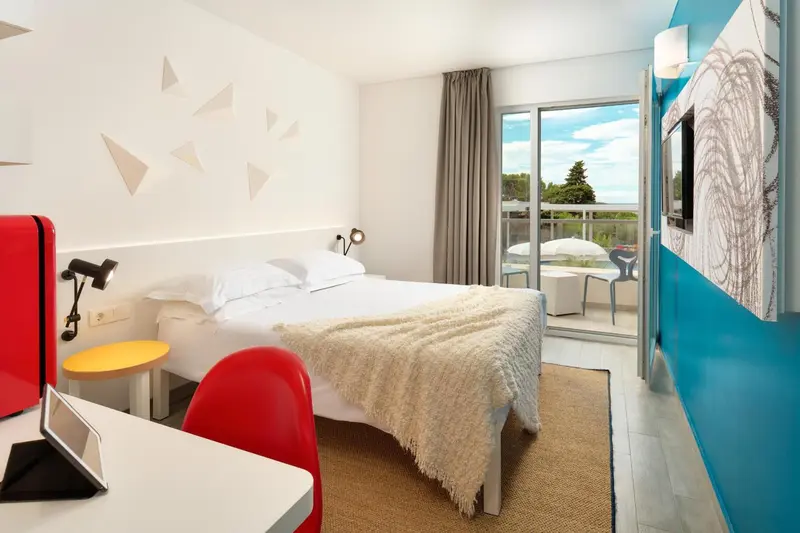 Chambre lumineuse avec un lit blanc et une terrasse ensoleillée.