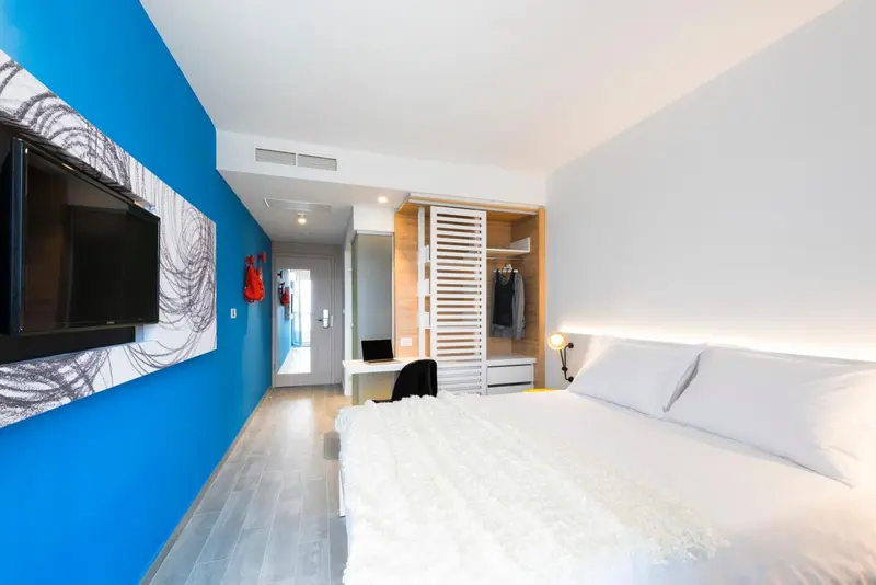 Une chambre lumineuse avec un grand lit blanc et un bureau.