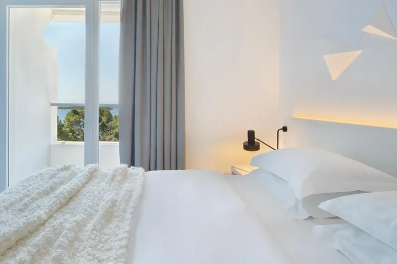 Une chambre lumineuse avec un grand lit blanc et une vue sur la mer.