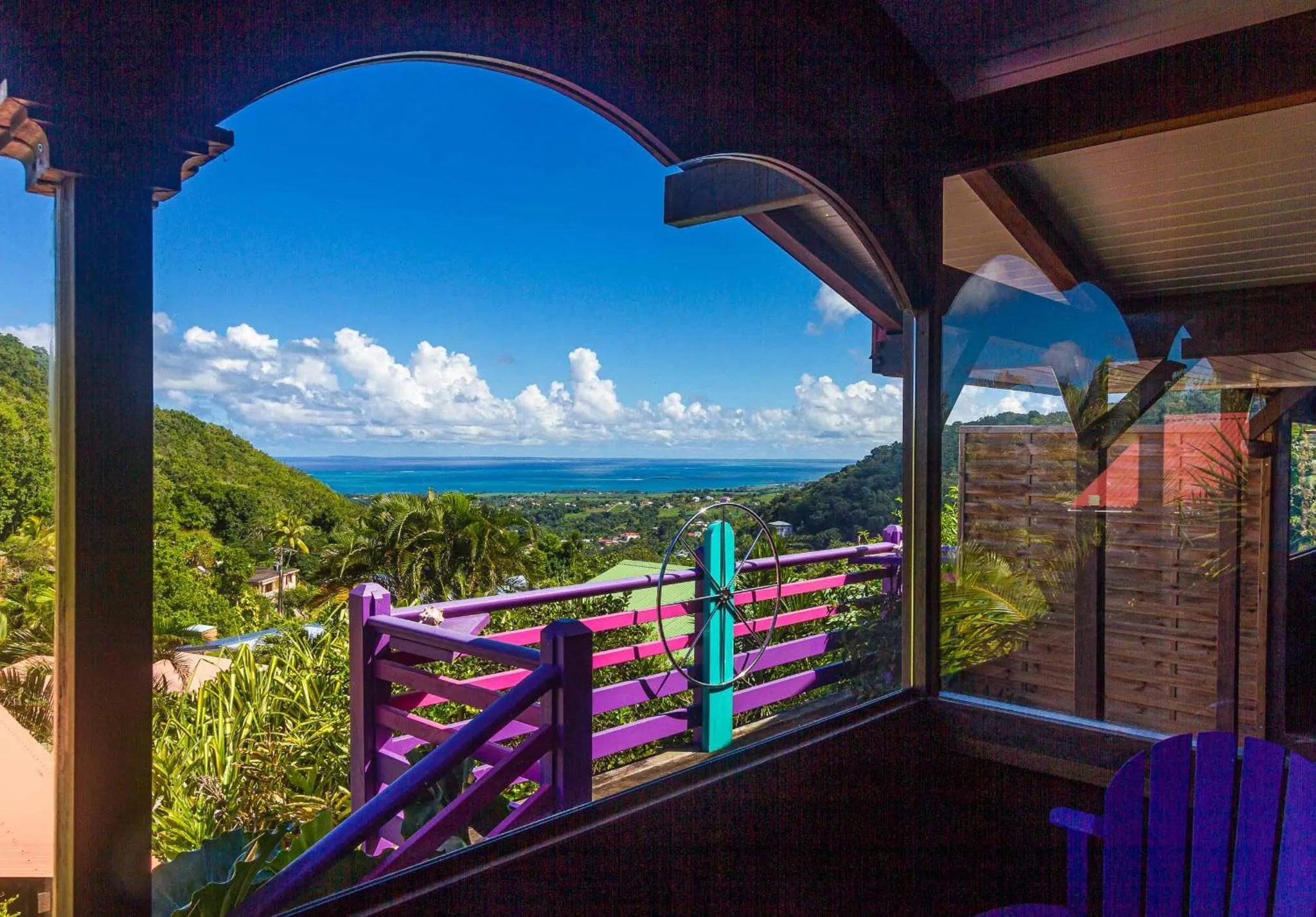 Vue dégagée sur une colline verdoyante et la mer depuis une terrasse ombragée.