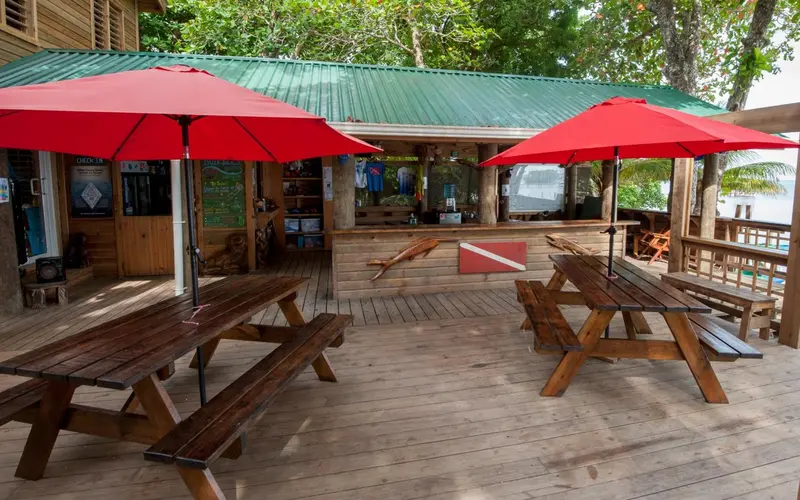 Terrasse en bois avec tables et parasols rouges devant un bâtiment ouvert.