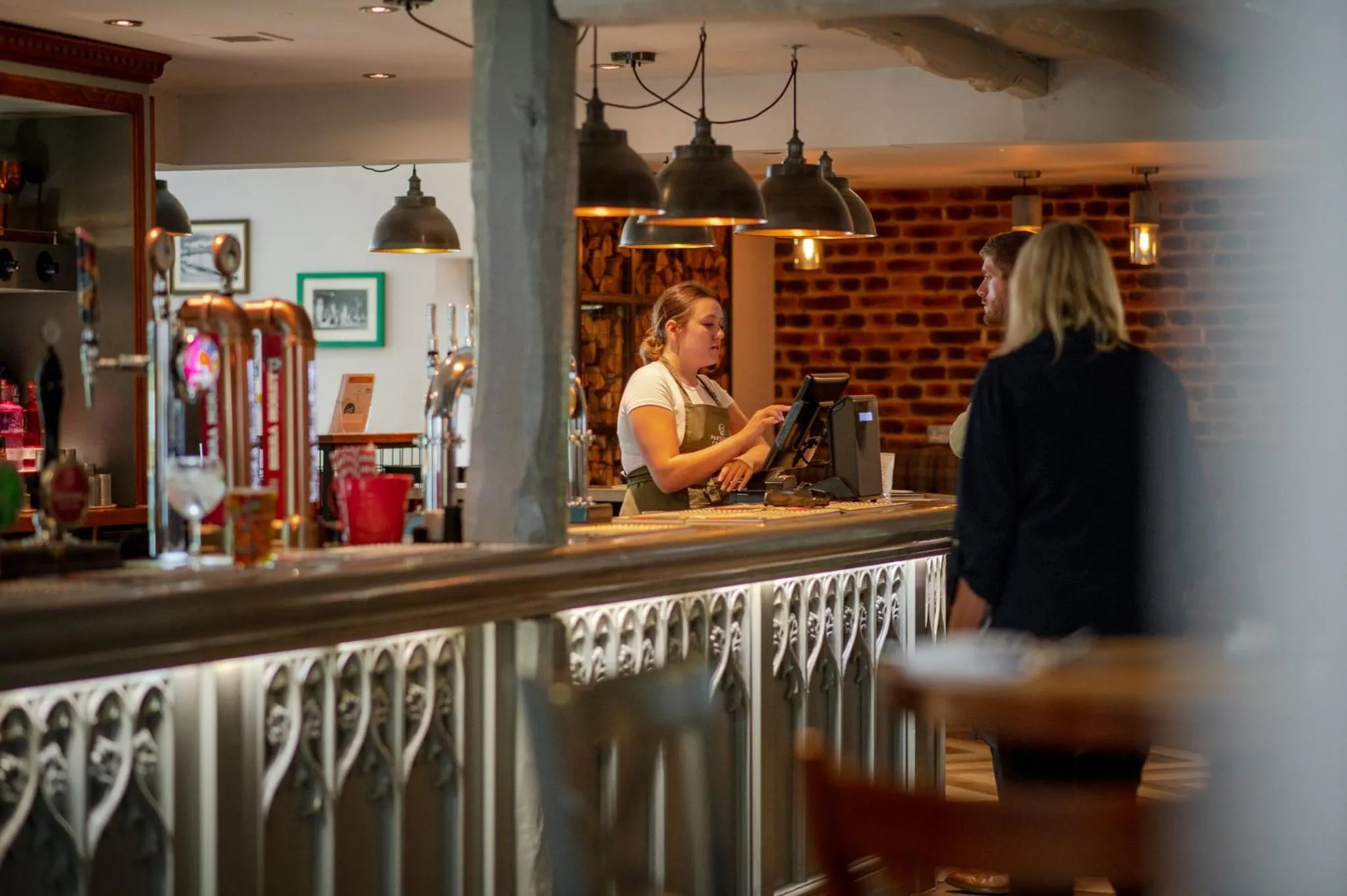 Une employée derrière un comptoir de bar accueille une cliente.