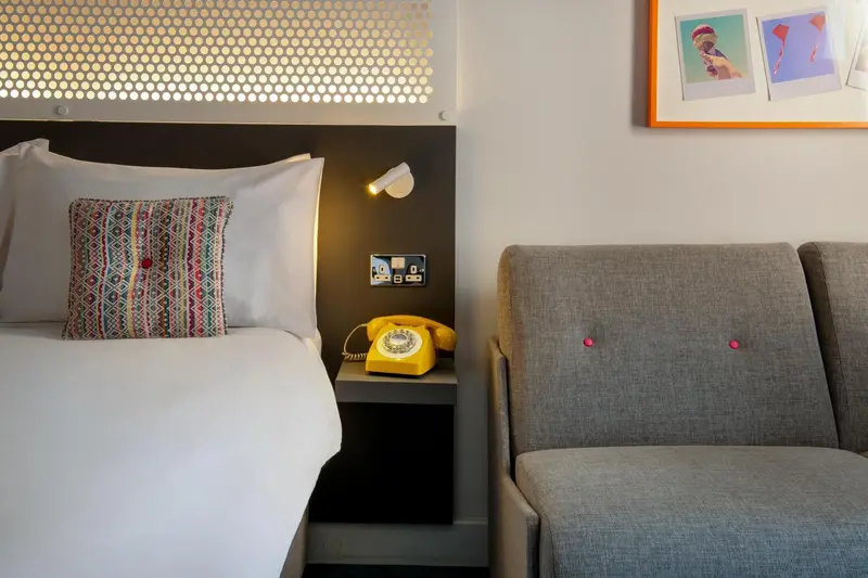 Une chambre lumineuse avec un lit fait et un fauteuil.