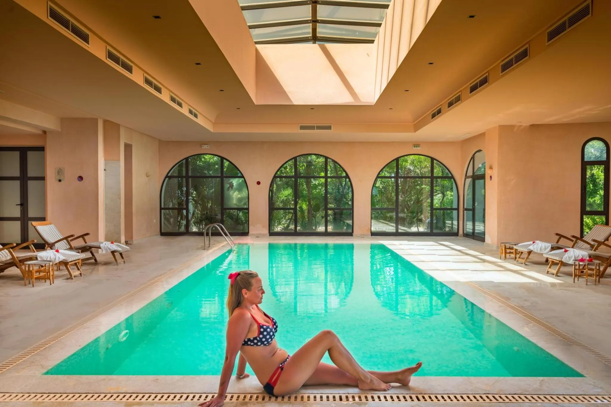 Une femme se détend au bord d'une piscine intérieure lumineuse.