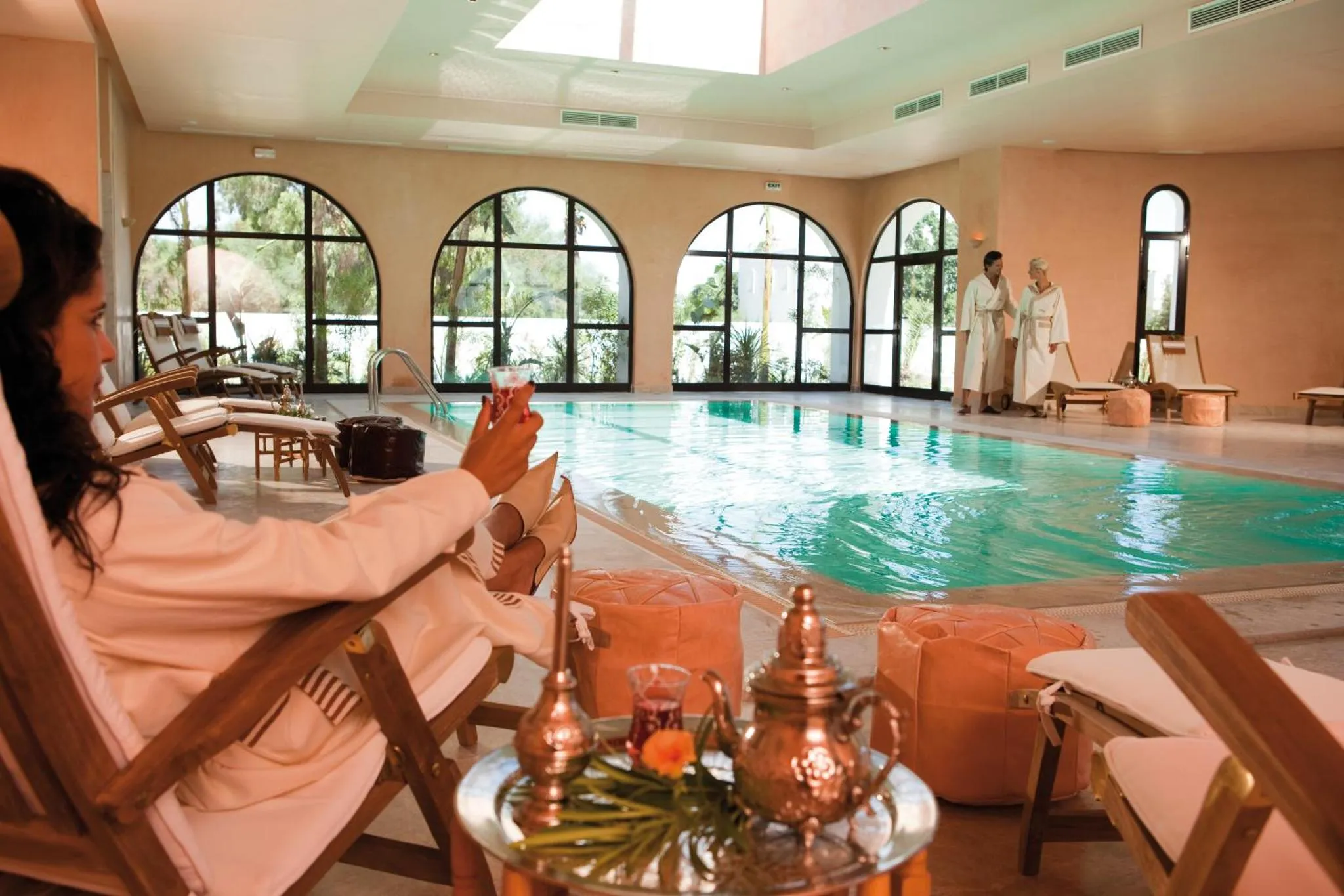 Une femme se détend sur une chaise longue au bord d'une piscine intérieure.