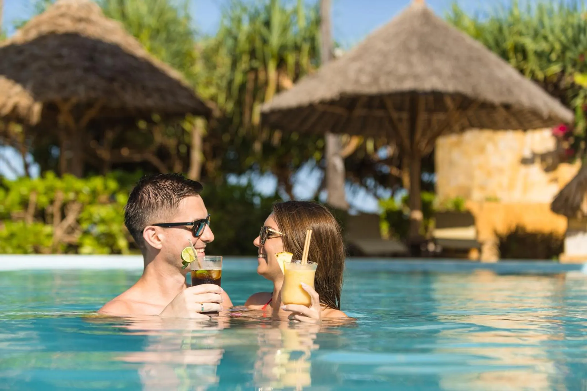 Un couple se détend dans une piscine en sirotant des boissons.