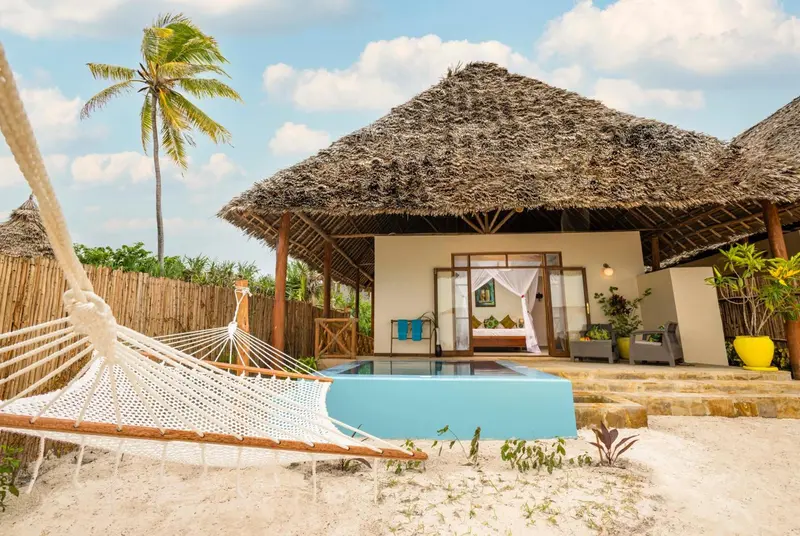 Une chambre avec un lit à baldaquin donnant sur une petite piscine et une plage de sable.
