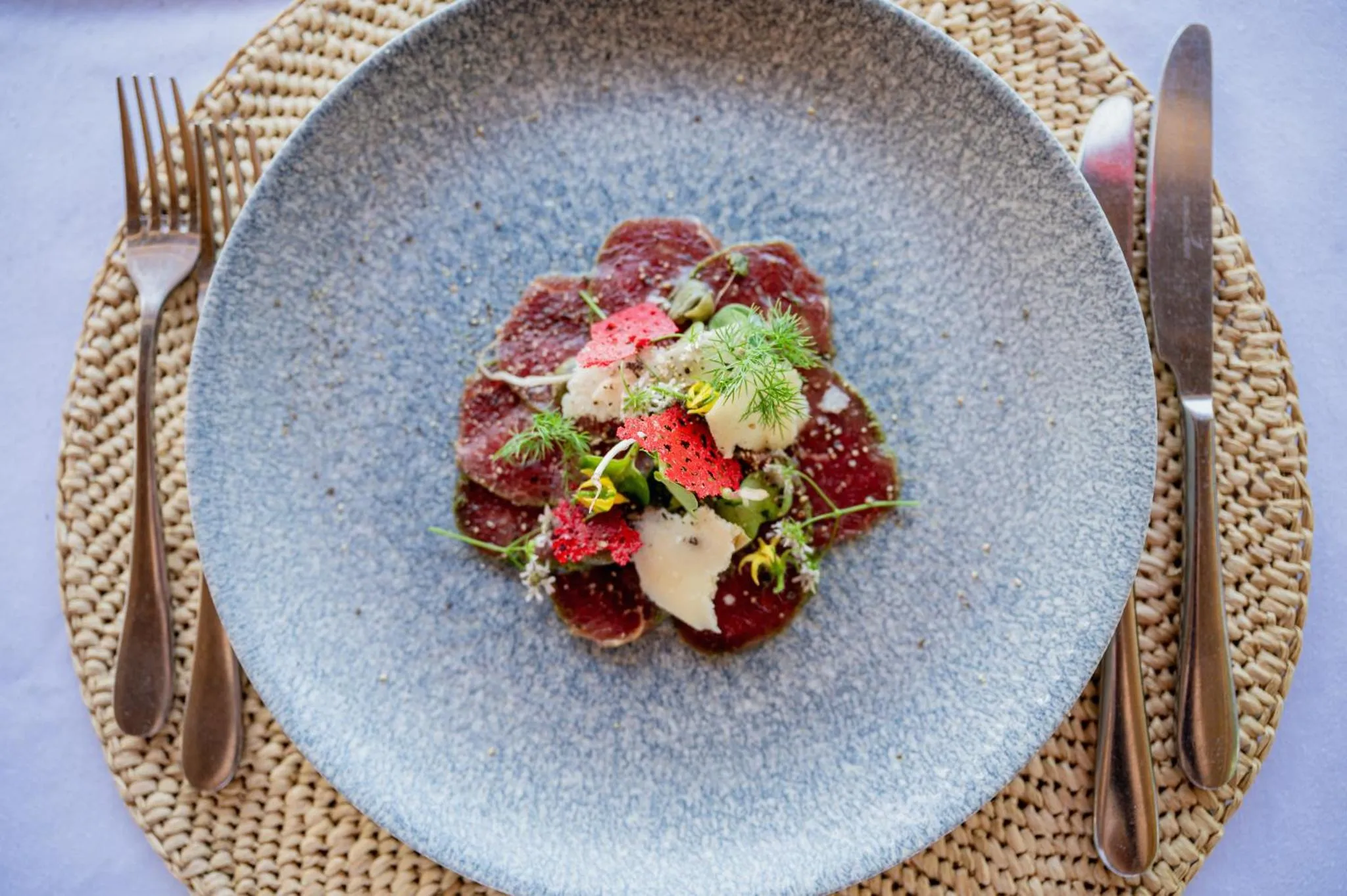 Assiette de fines tranches de viande rouge, décorée de légumes et d'herbes.