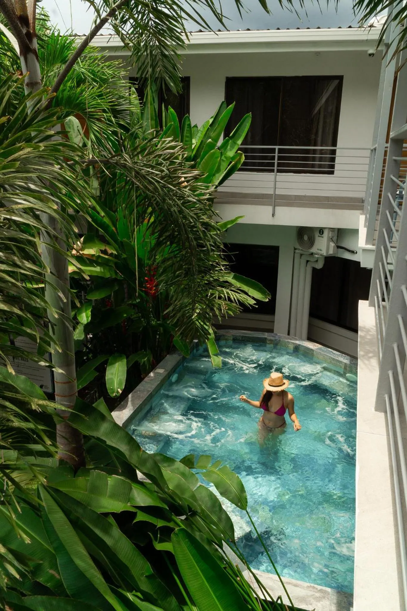 Une personne se détend dans une piscine entourée de végétation tropicale.