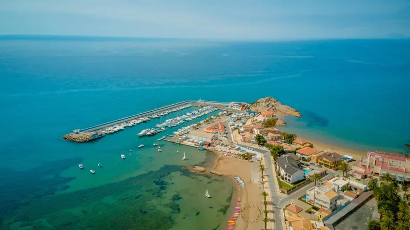 Vue aérienne d'une côte rocheuse avec un port de plaisance et une plage.