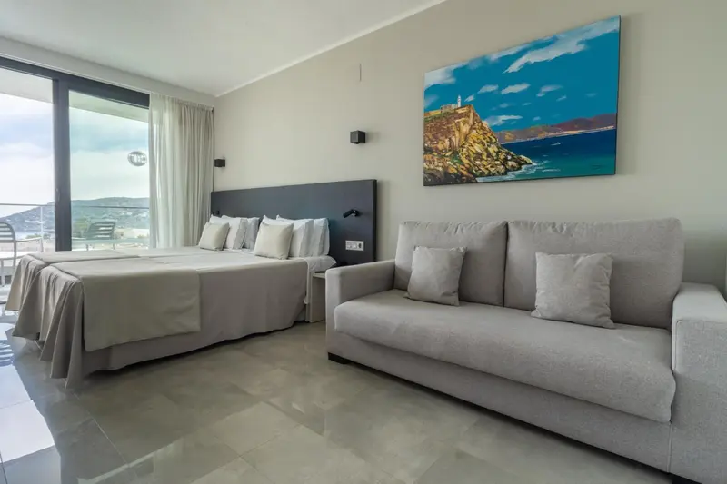 Espace de vie lumineux avec canapé et lit face à une grande baie vitrée.