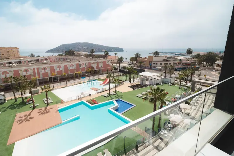 Vue aérienne sur une piscine et un complexe hôtelier avec la mer en arrière-plan.