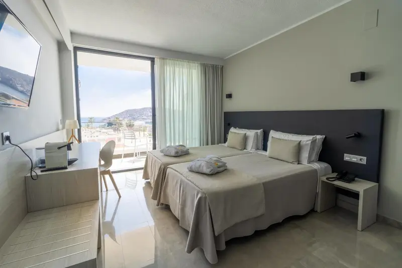 Chambre lumineuse avec deux lits simples et vue sur la mer.