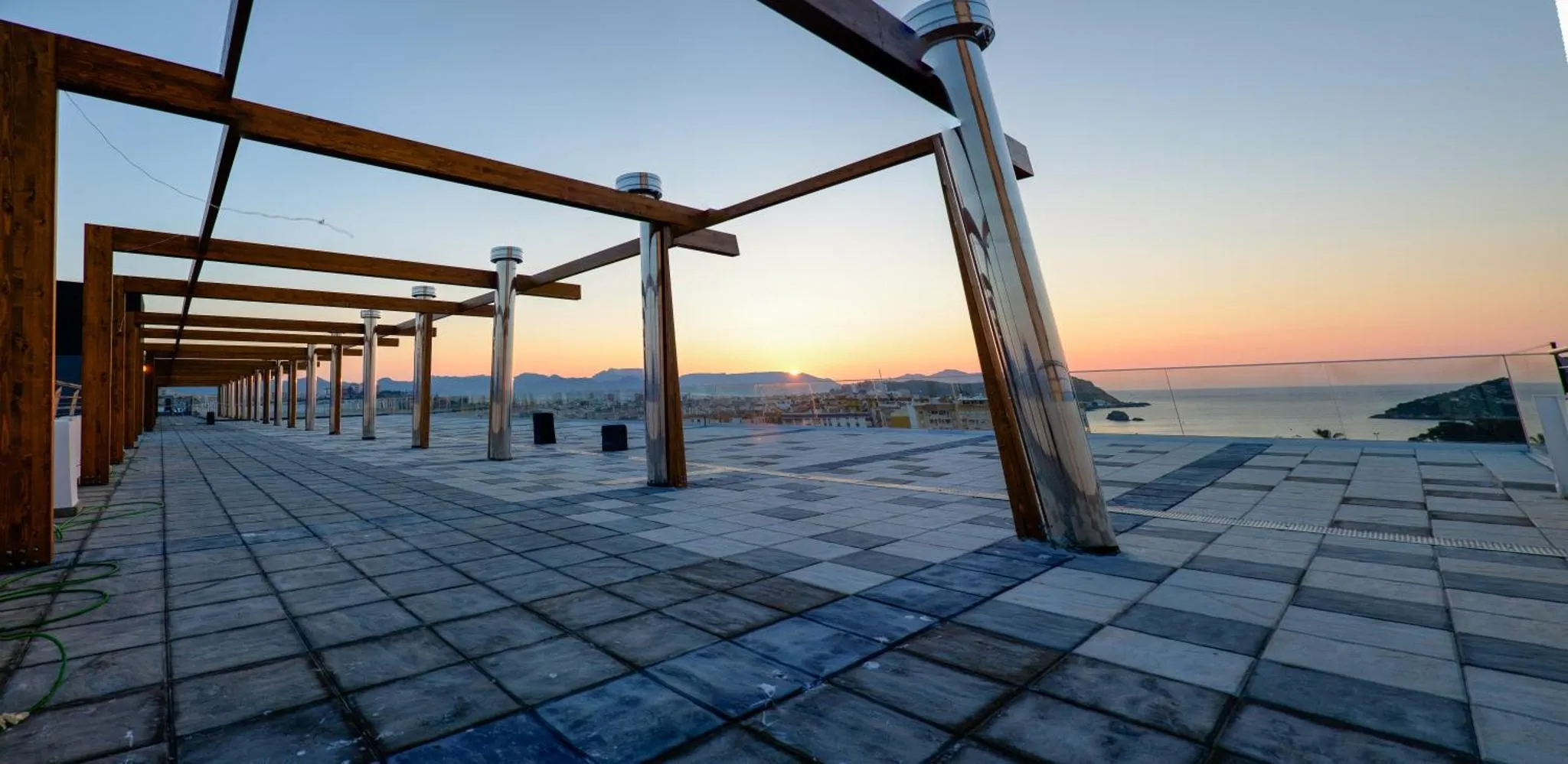 Terrasse carrelée avec une structure en bois et vue sur la mer au coucher du soleil.