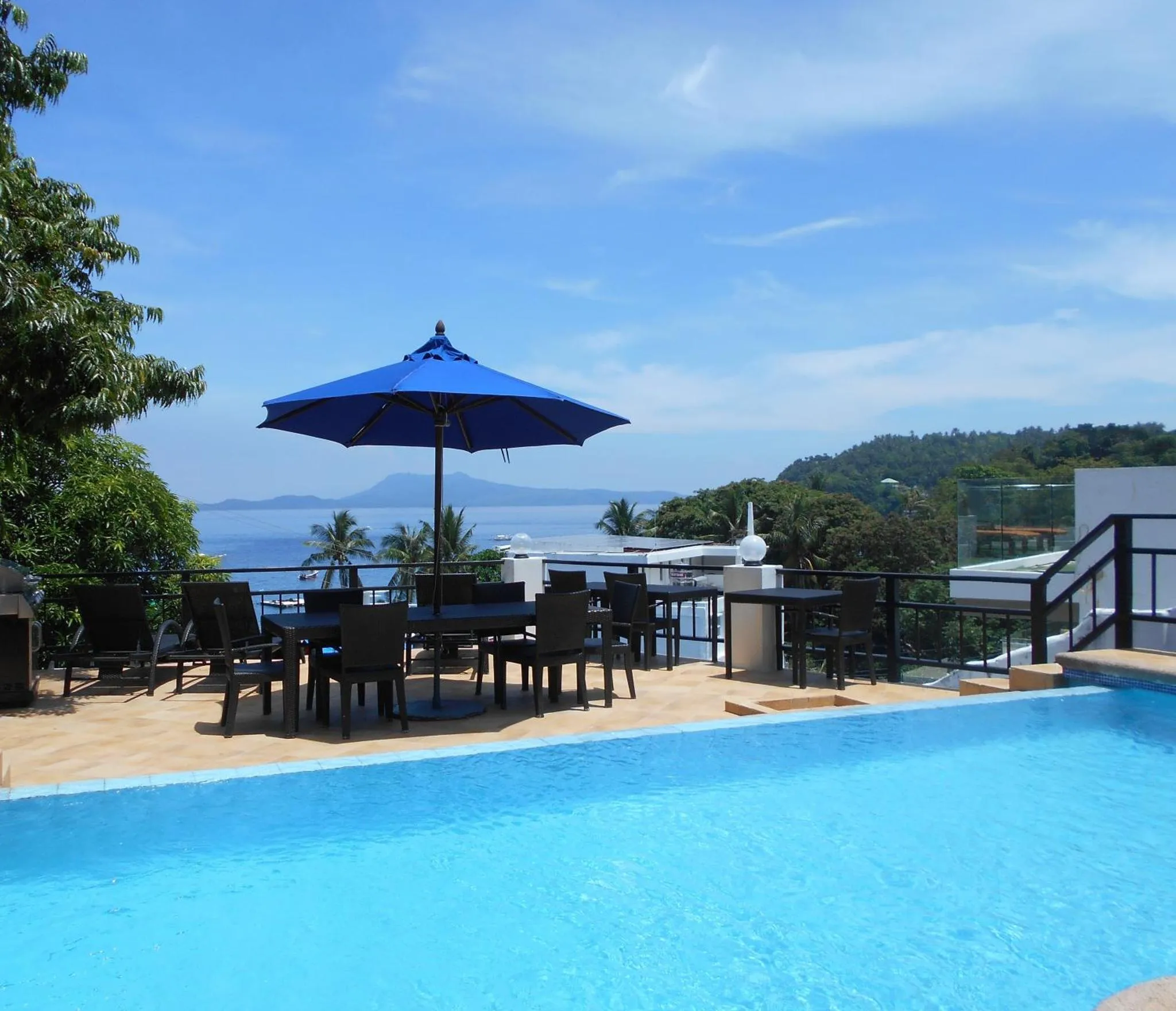 Terrasse avec tables et chaises près d'une piscine et vue sur la mer.