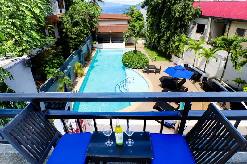 Terrasse avec table basse et boissons, surplombant une piscine et un jardin tropical.