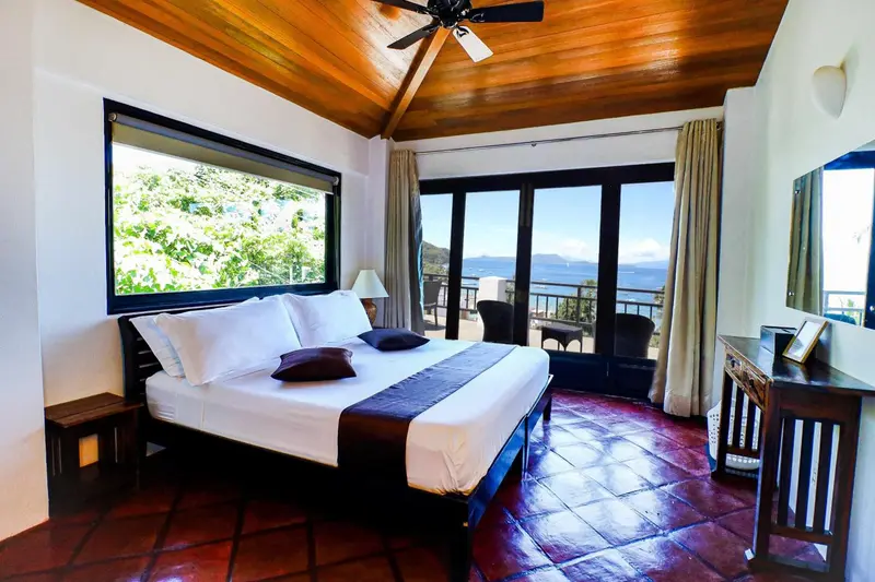Une chambre lumineuse avec un grand lit donnant sur une vue mer.