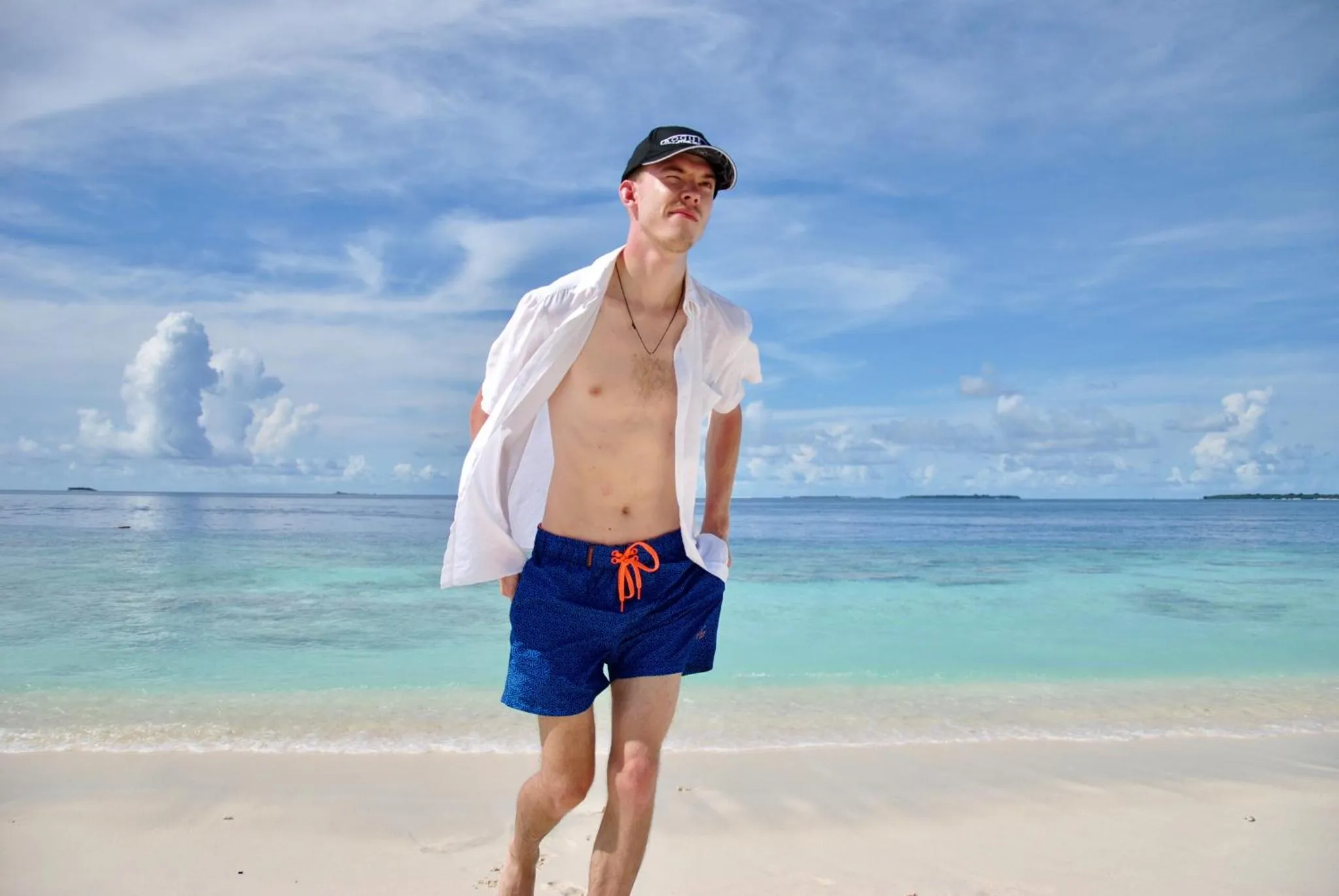 Un homme se tient sur une plage de sable blanc face à la mer turquoise.