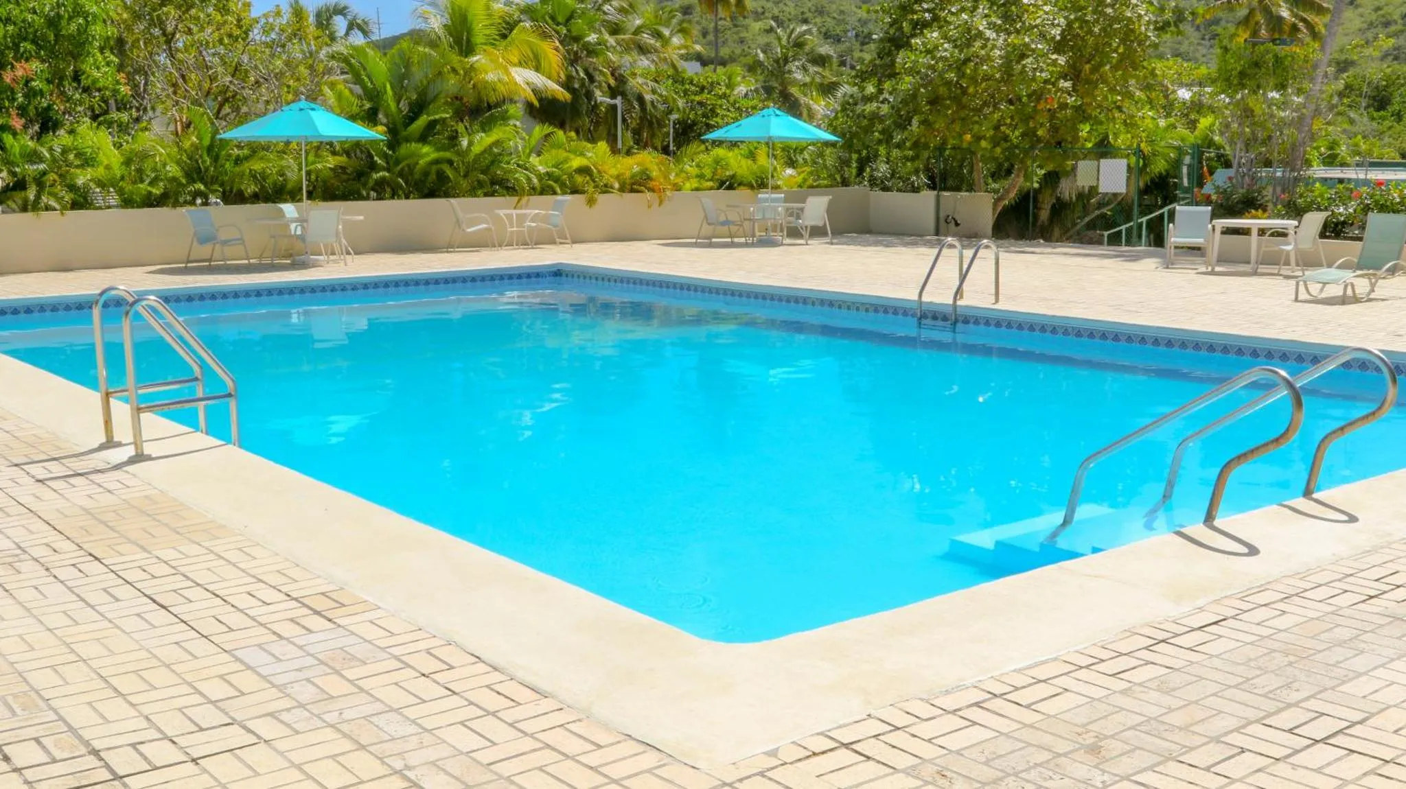 Une piscine rectangulaire entourée d'une terrasse pavée avec des transats bleus et des parasols.