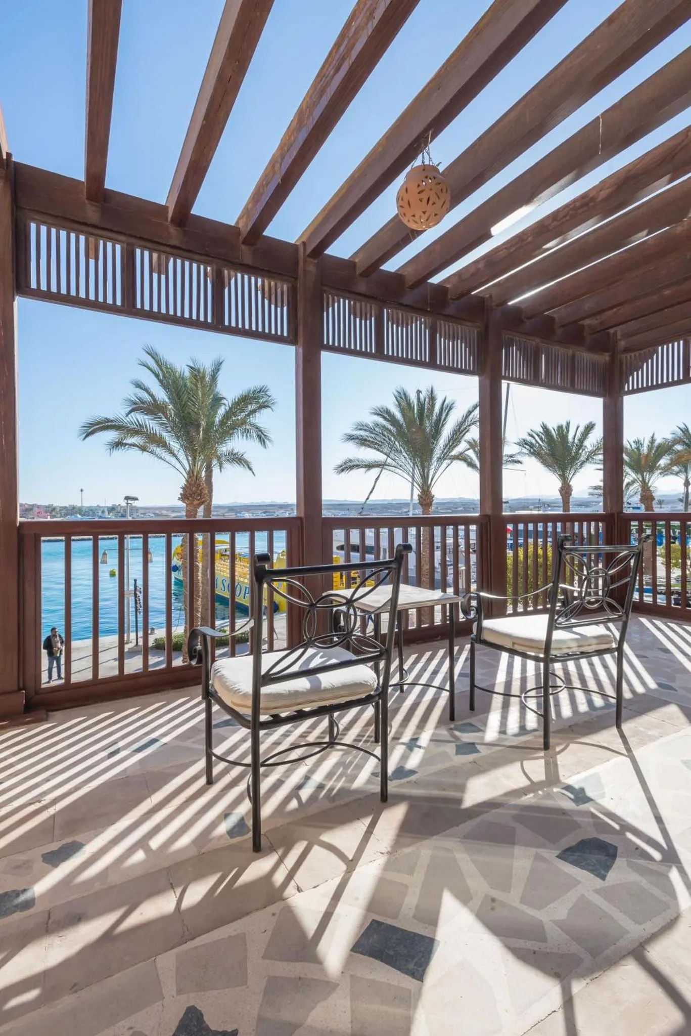 Terrasse ombragée avec mobilier de jardin donnant sur la mer et des palmiers.