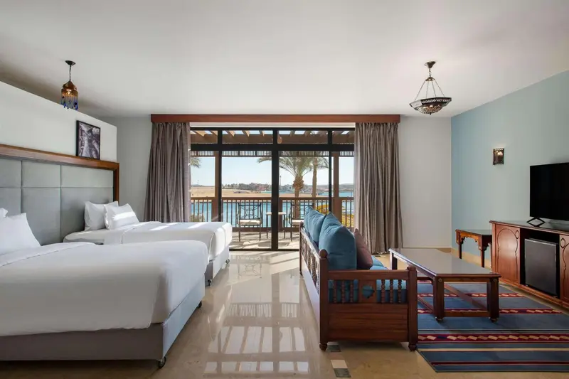 Une chambre lumineuse avec deux lits et un canapé face à une baie vitrée.