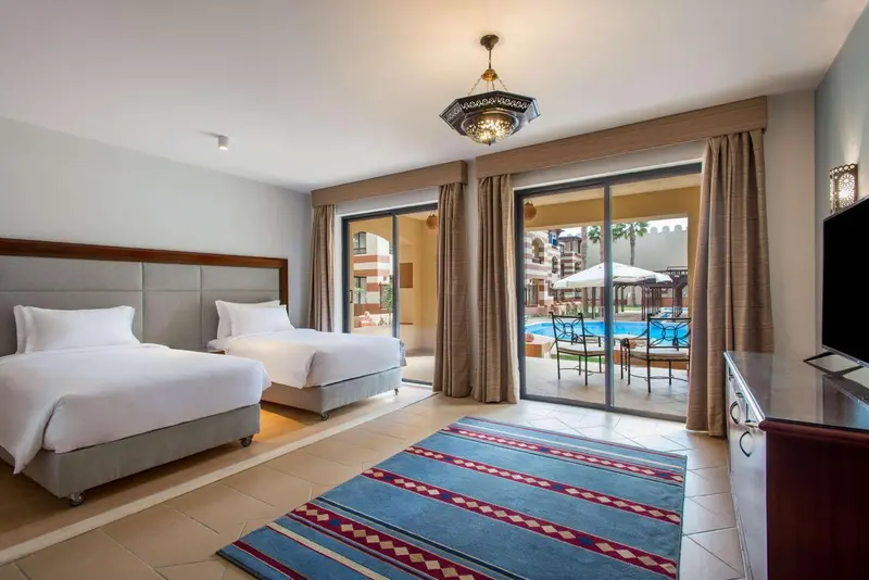 Chambre lumineuse avec deux lits simples donnant sur une piscine.