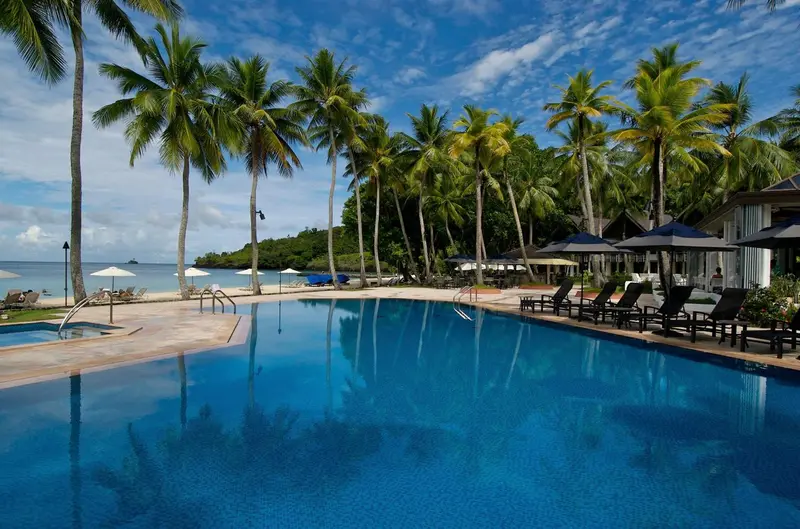 Une piscine turquoise reflète les palmiers et le ciel bleu.