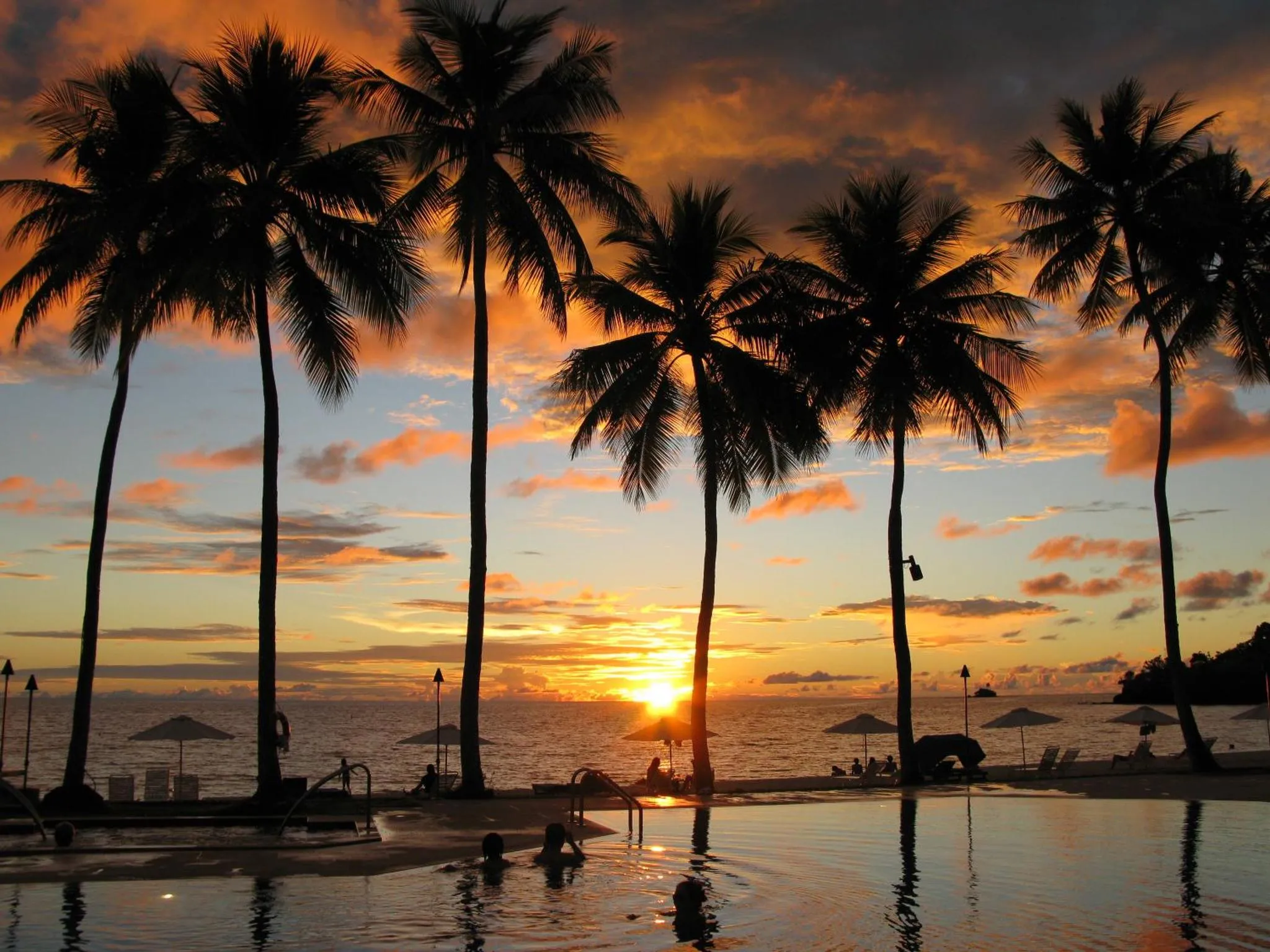 Coucher de soleil sur une plage avec des palmiers et une piscine.