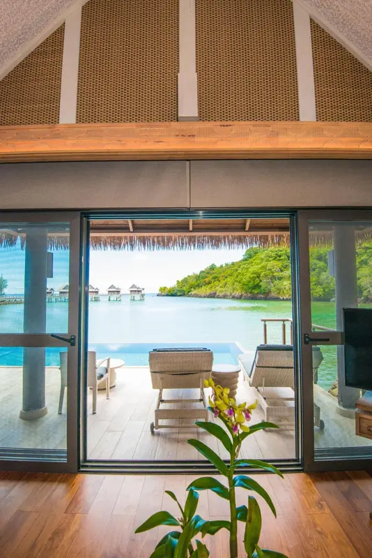Vue sur une terrasse avec des fauteuils et une piscine depuis un intérieur lumineux.
