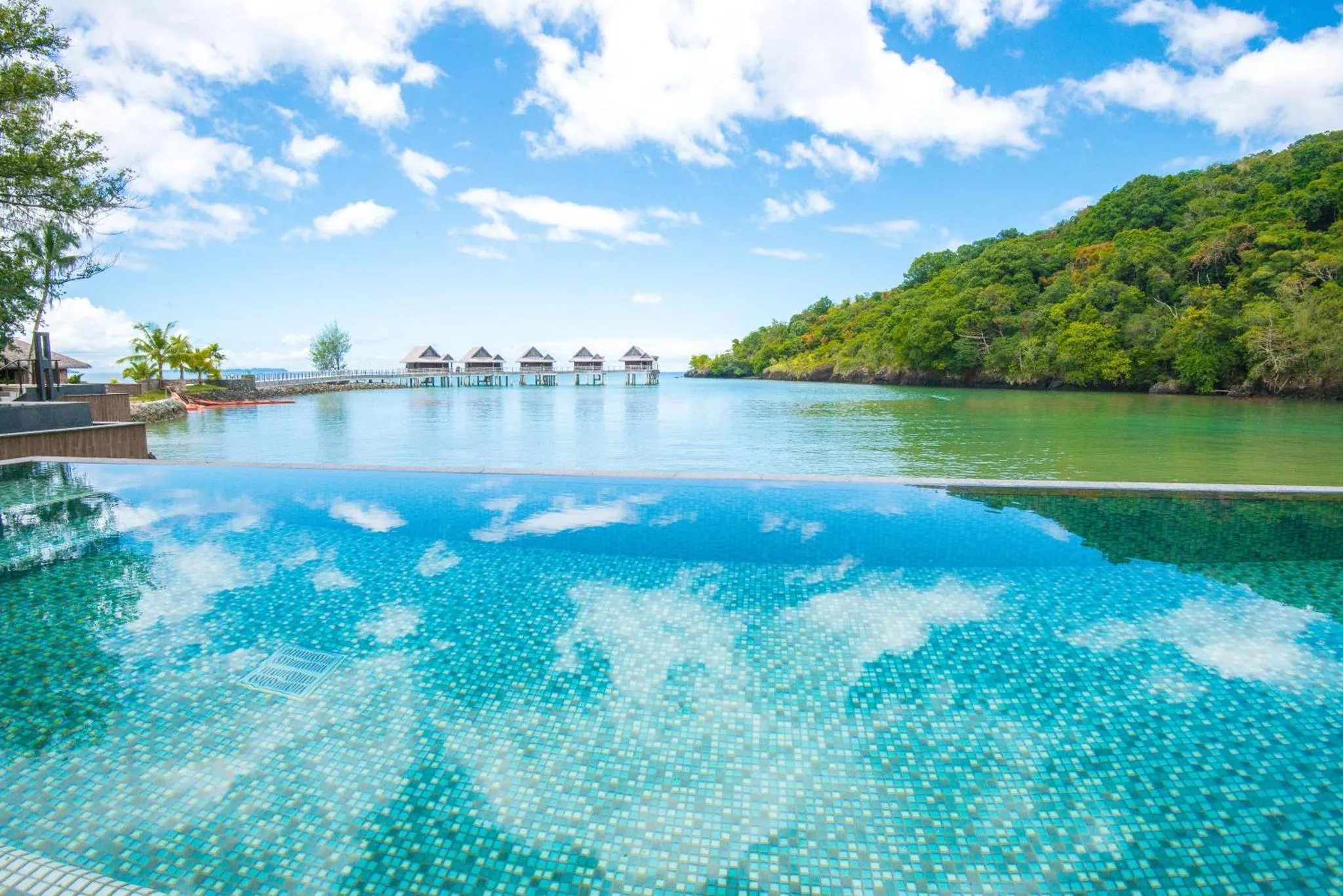 Une piscine à débordement offre une vue sur la mer et la végétation luxuriante.