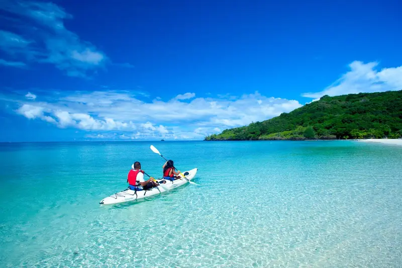 Deux personnes pratiquent le kayak sur une eau turquoise et calme.