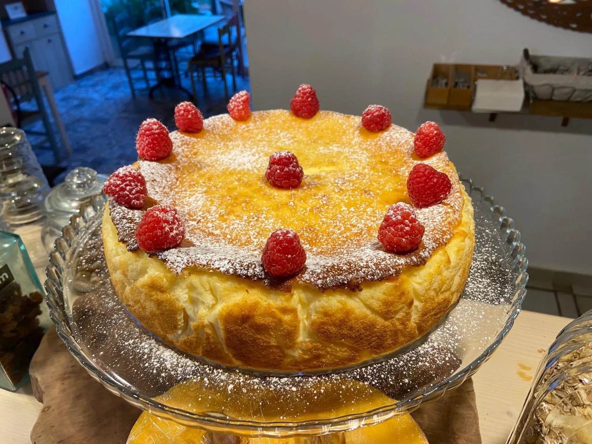 Un gâteau au fromage décoré de framboises est présenté sur un présentoir.