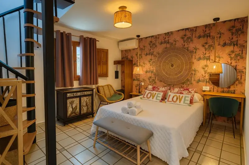 Une chambre à coucher lumineuse avec un lit décoré de coussins et un escalier en colimaçon.