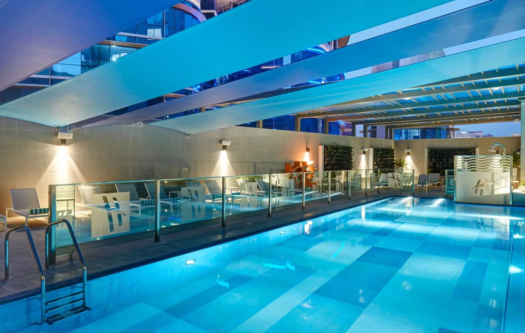 Piscine intérieure illuminée avec transats et barrière de verre.