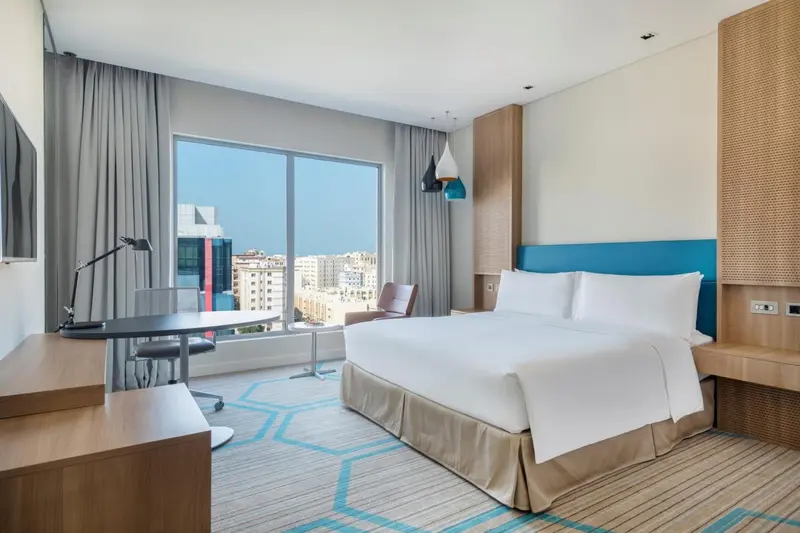 Chambre lumineuse avec un grand lit et un bureau près de la fenêtre.