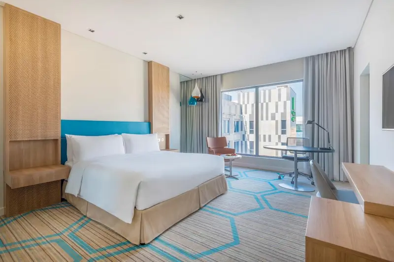 Chambre lumineuse avec un grand lit et un bureau près de la fenêtre.