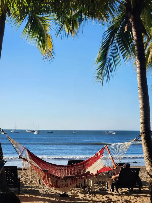 Un hamac rouge est suspendu entre deux palmiers sur une plage de sable.