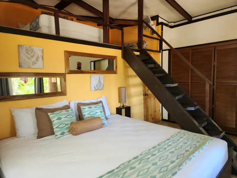Une chambre lumineuse avec un lit et un escalier menant à une mezzanine.