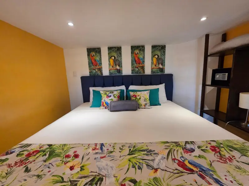 Une chambre lumineuse avec un grand lit recouvert d'une couette blanche et de motifs tropicaux.