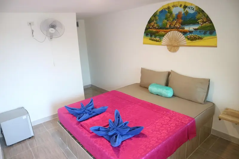 Une chambre lumineuse avec un lit recouvert d'un drapé coloré et un ventilateur au plafond.