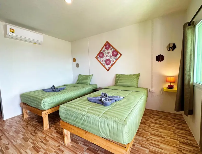 Une chambre lumineuse avec deux lits simples verts et une décoration murale colorée.