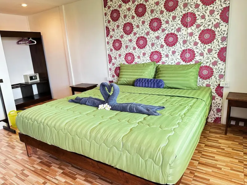 Une chambre lumineuse avec un lit recouvert d'une couette verte et décoré de serviettes en forme de cygnes.