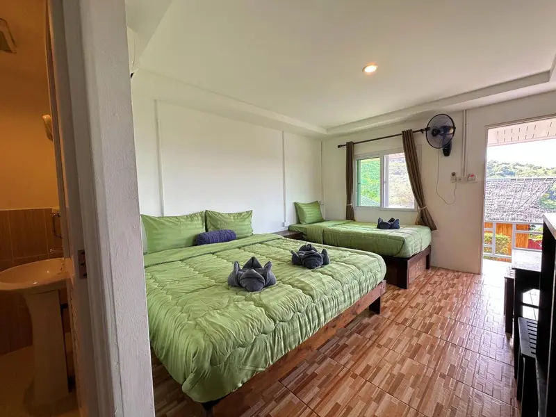 Chambre lumineuse avec deux lits verts et une vue sur la végétation.