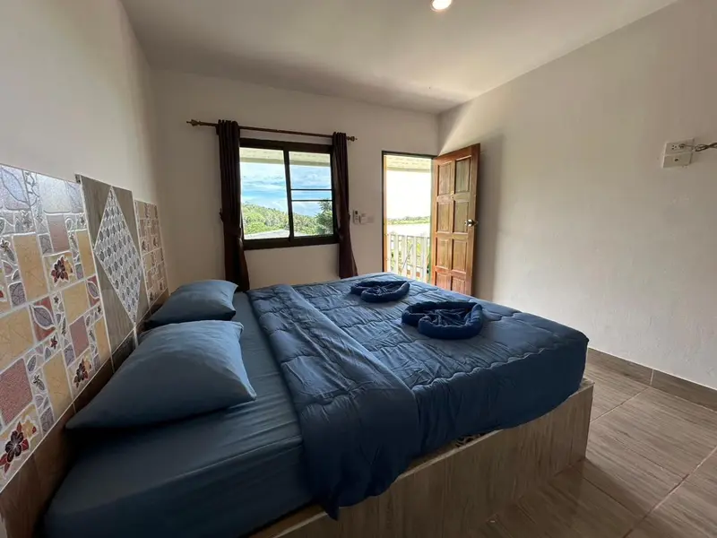 Une chambre lumineuse avec un grand lit recouvert d'une couverture bleue et donnant sur une terrasse.