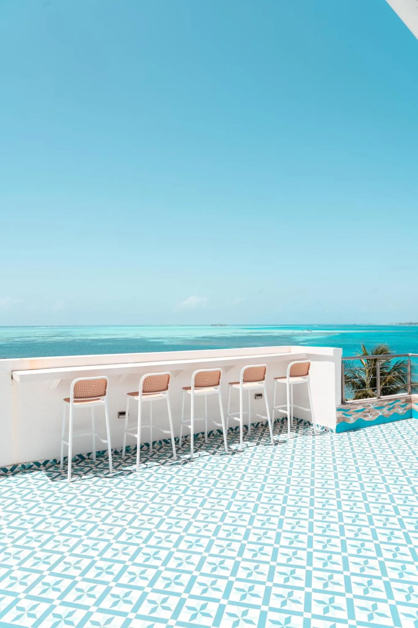 Terrasse carree avec des tabourets de bar blancs et une vue sur la mer turquoise.