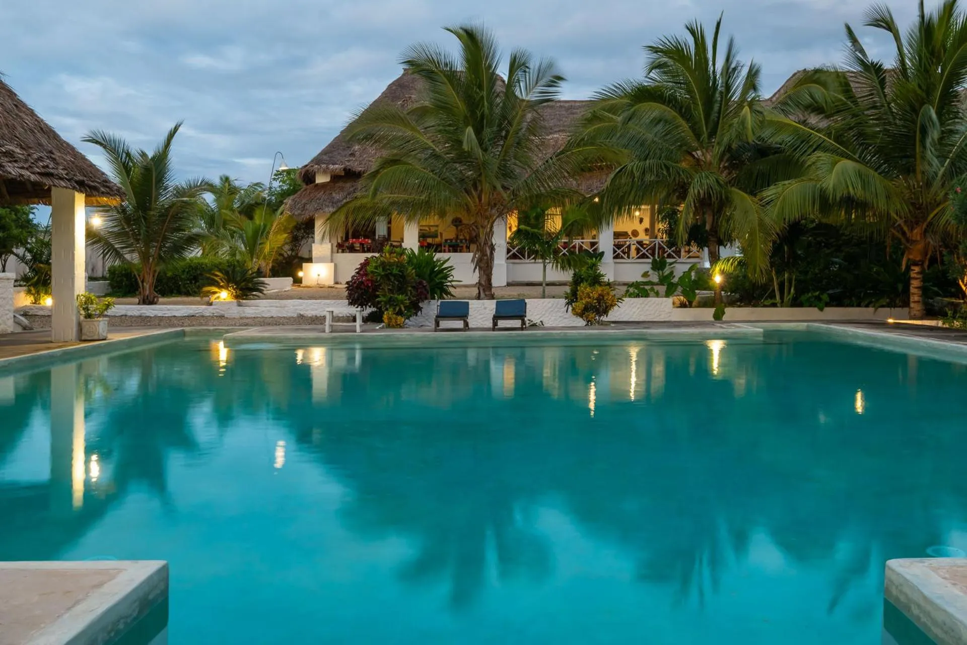 Piscine turquoise reflétant les lumières d'un bâtiment tropical au crépuscule.