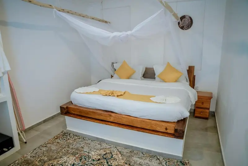 Lit à baldaquin avec linge blanc et coussins jaunes dans une chambre décorée.