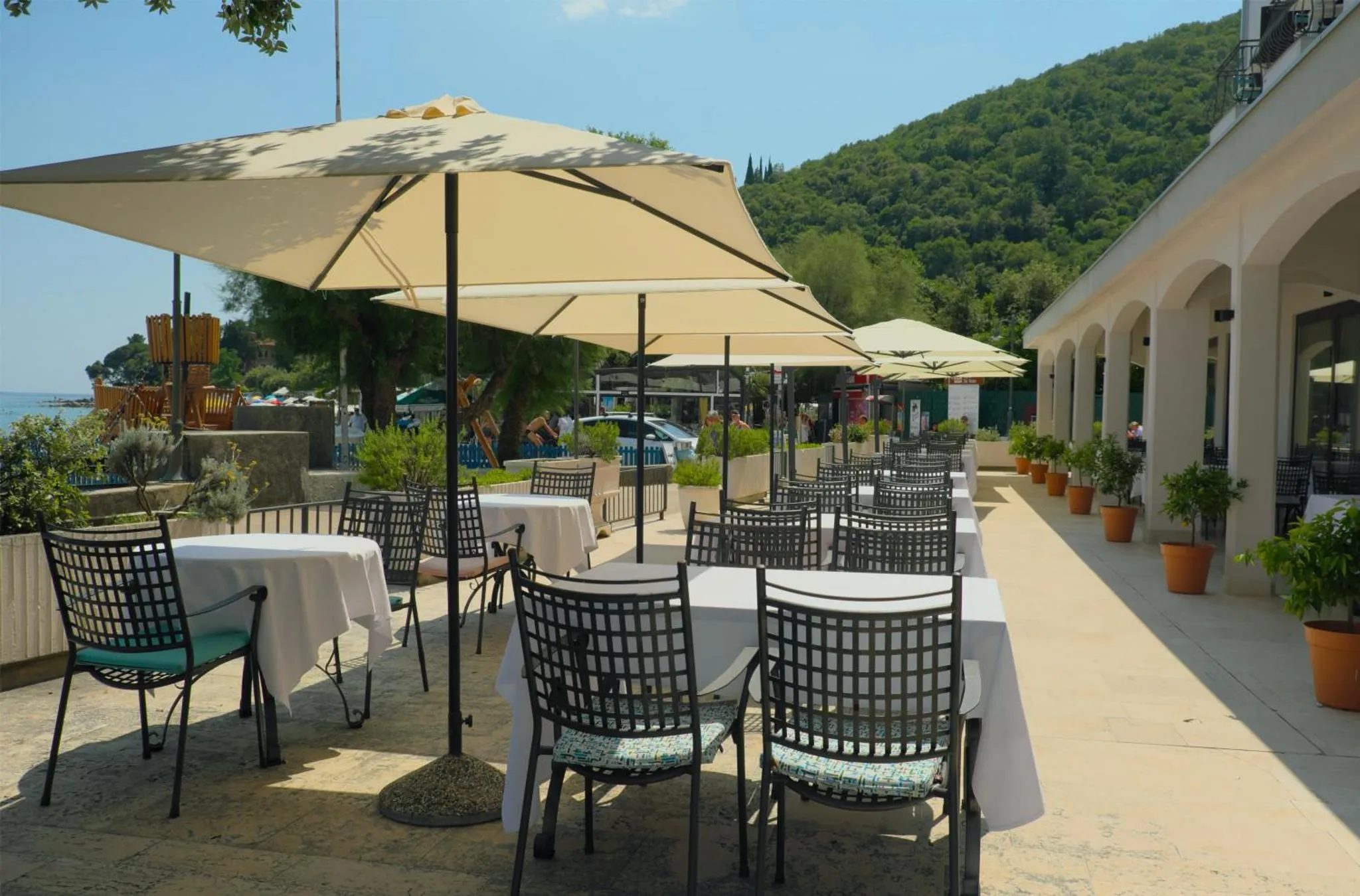 Terrasse ombragée avec tables et chaises en fer forgé, vue sur la mer.